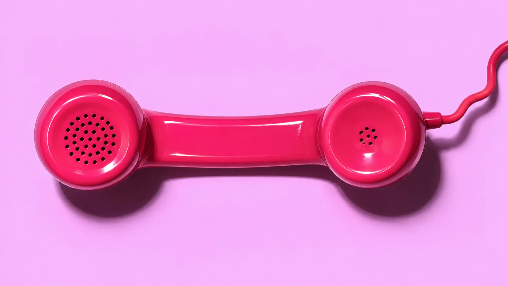 Comuniqa — telefone pink em fundo lilás Auscultador de telefone pink, na horizontal, sobre fundo lilás numa composição editorial da Comuniqa